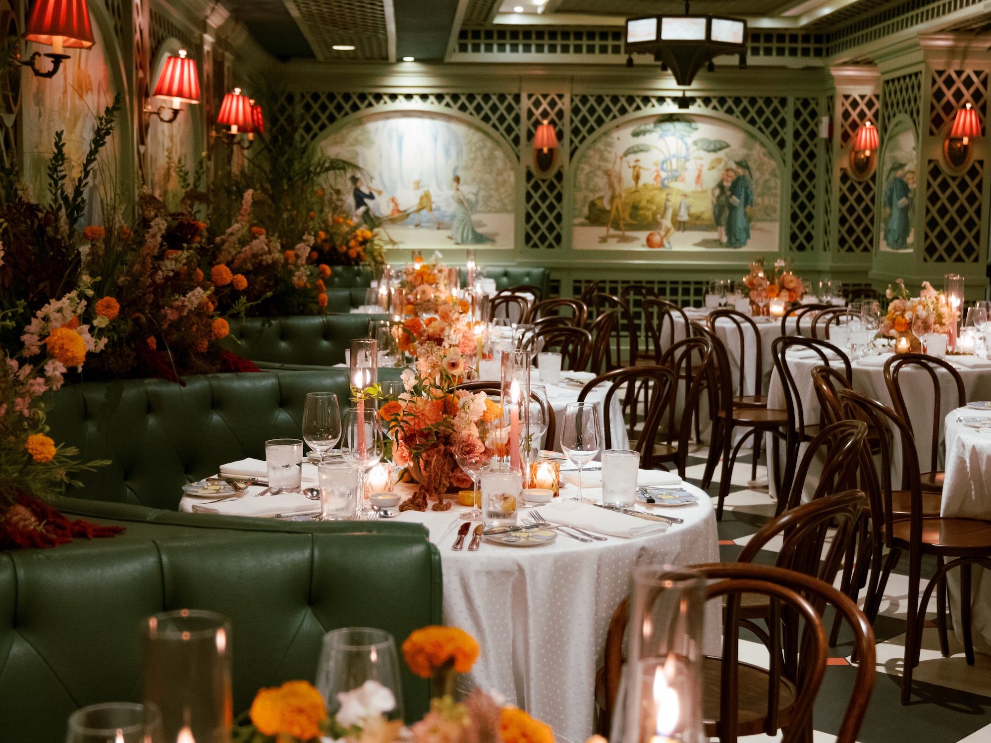 Tables in a green dining room set with orange florals and pink taper candles