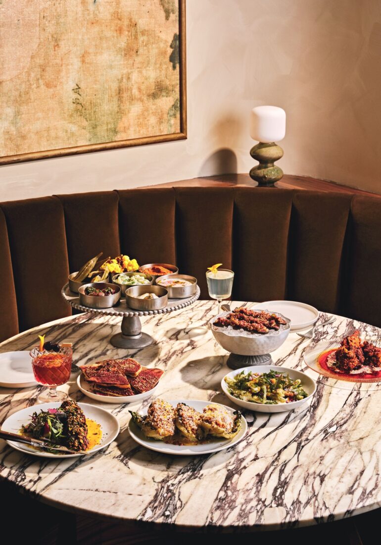 A table with a meze platter, grilled short rib, Venetian-style artichoke, grilled little gem salad, and razor clams.