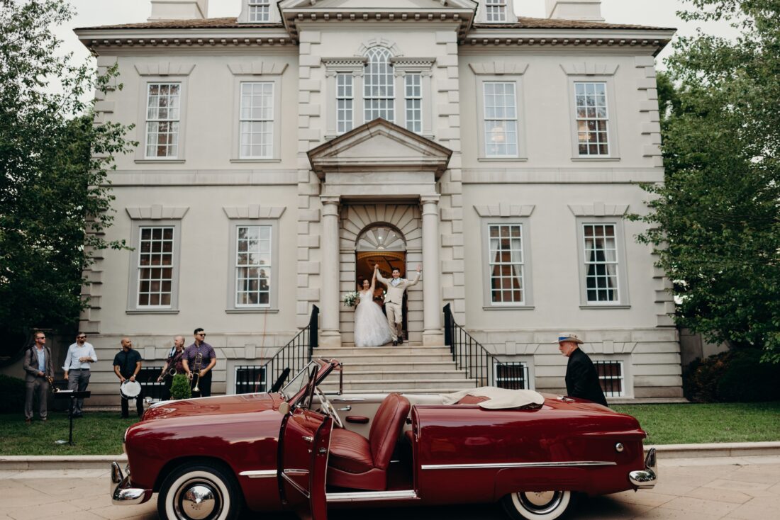 a bride and groom exit a church in front of a custom Ford convertible