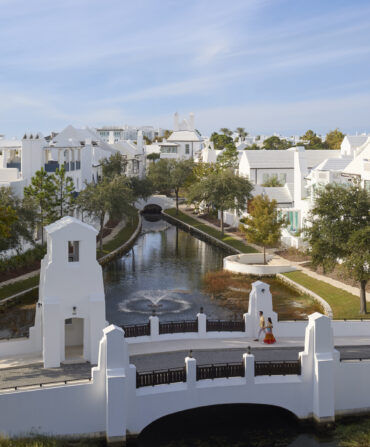 People walk over a small walking bridge in a white-painted villa