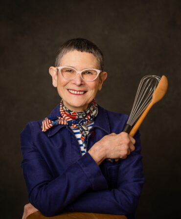 A portrait of a woman holding a whisk and wooden spoon