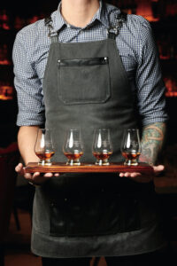A man holds a flight of whiskey on a wood board
