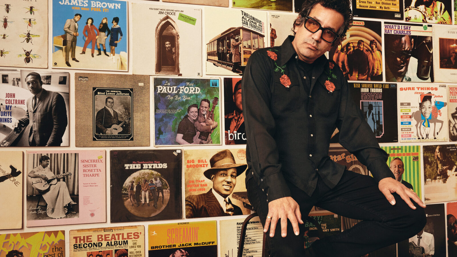 A man sits on a chair by a wall of records