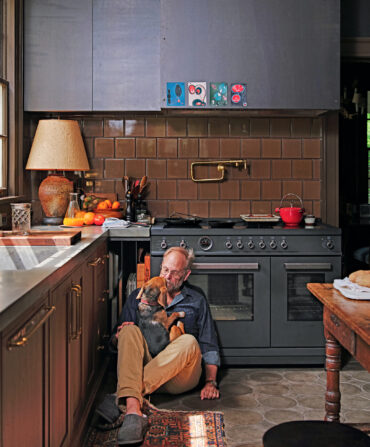 A man sits on a kitchen floor with a beagle in his lap