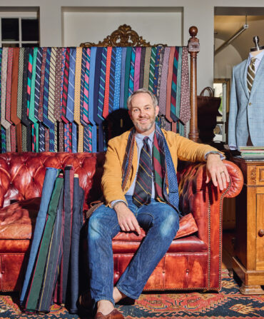 A portrait of a man in a clothing store. He wears ties around his neck