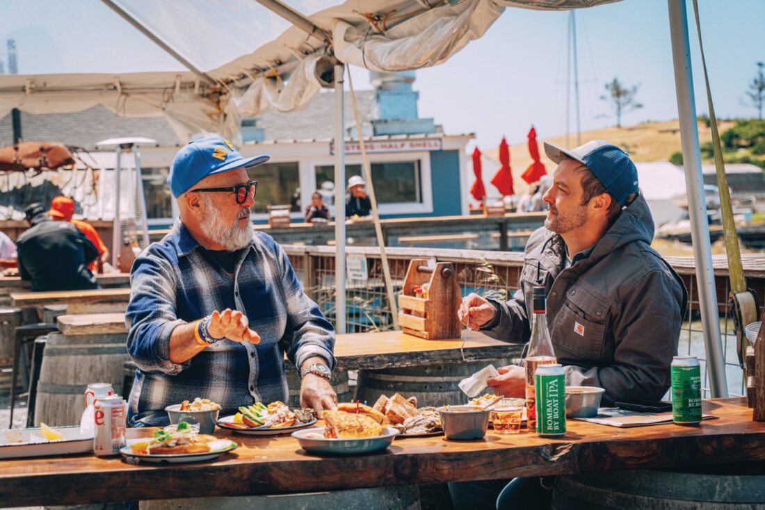 Two men sit at a table with fried seafood outside