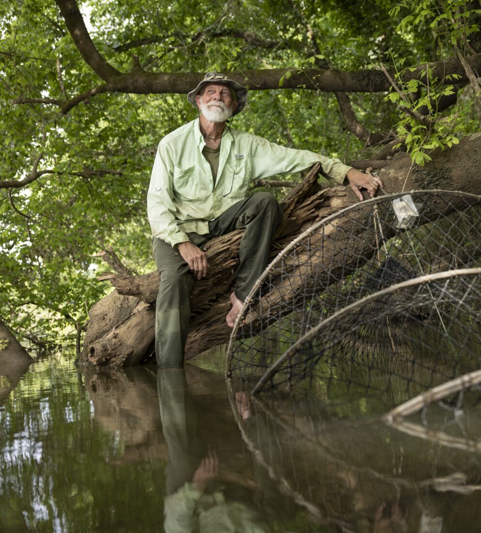 A man sits on a tree in a river by large nets