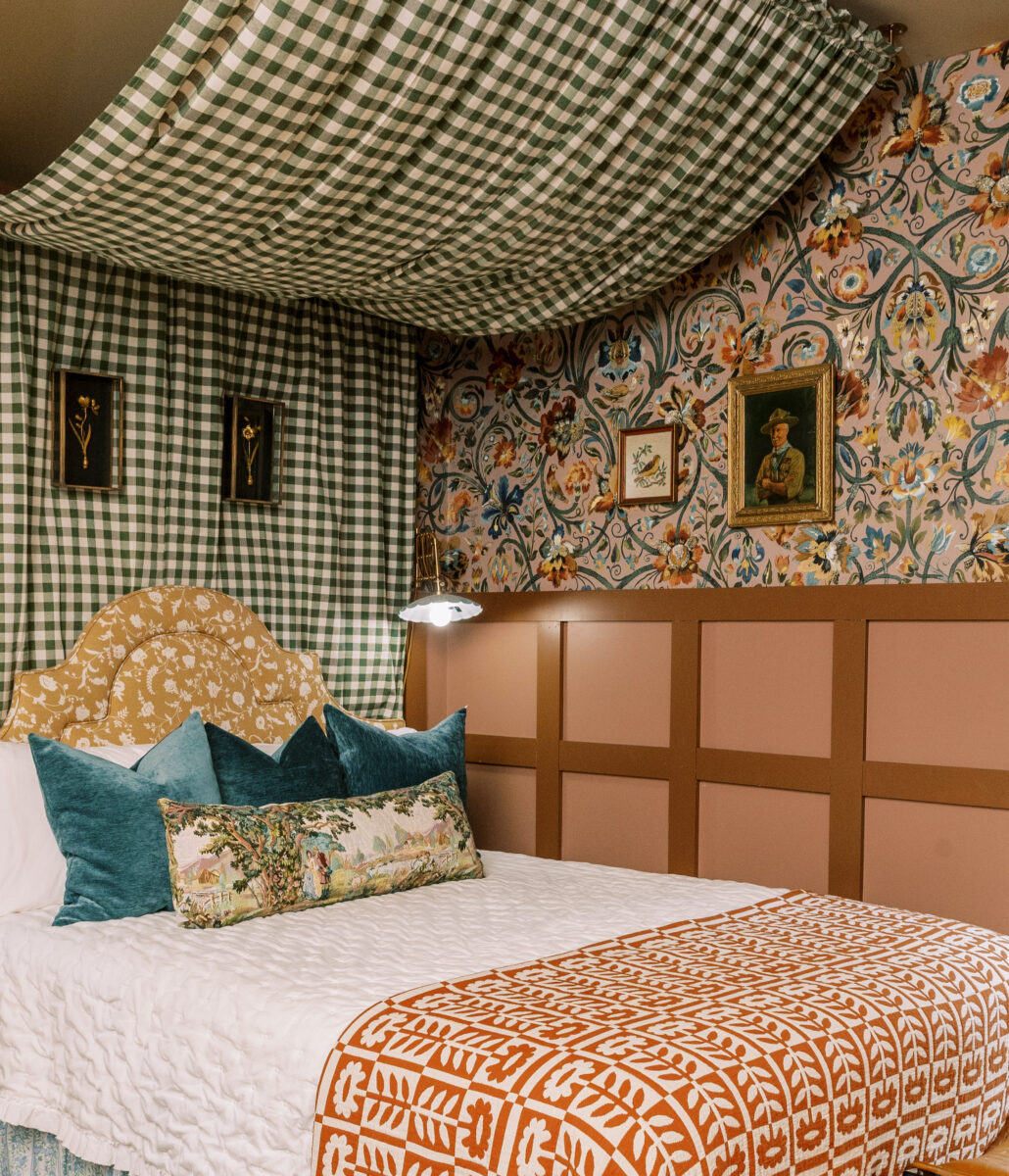 A plaid bed curtain over a bed in a room with floral wallpaper